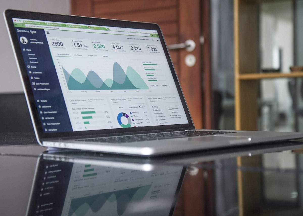 A laptop on a glass desk showing a dashboard with charts